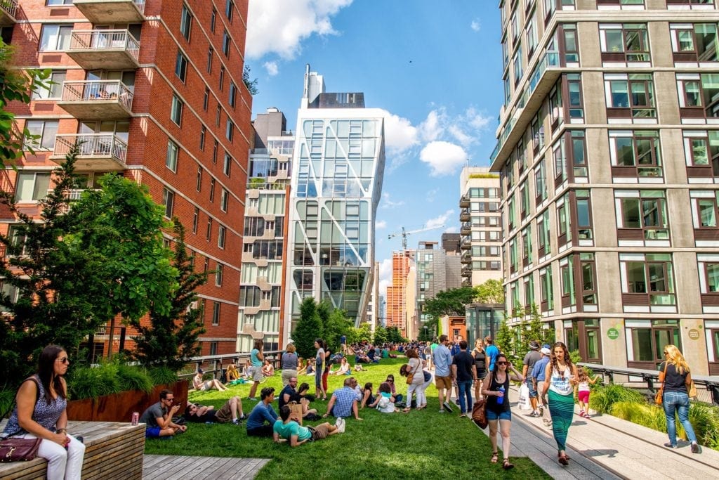 A group of people sitting on the grass in front of some buildings.
