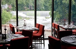 A restaurant with red chairs and tables near the water.