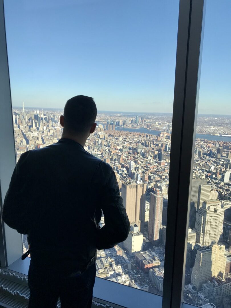 A man standing in front of a window looking at the city.