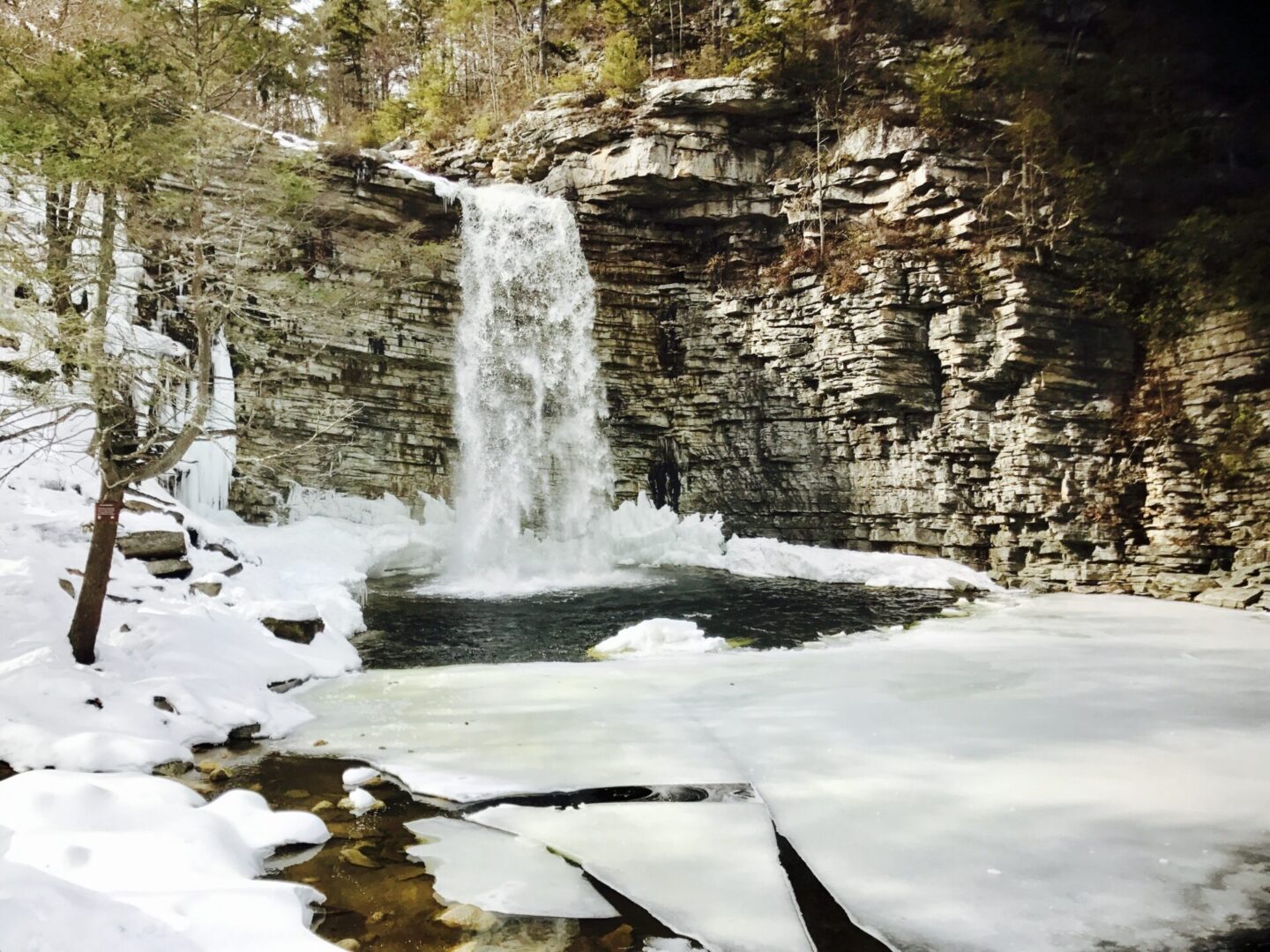 A waterfall is shown in the middle of a frozen lake.