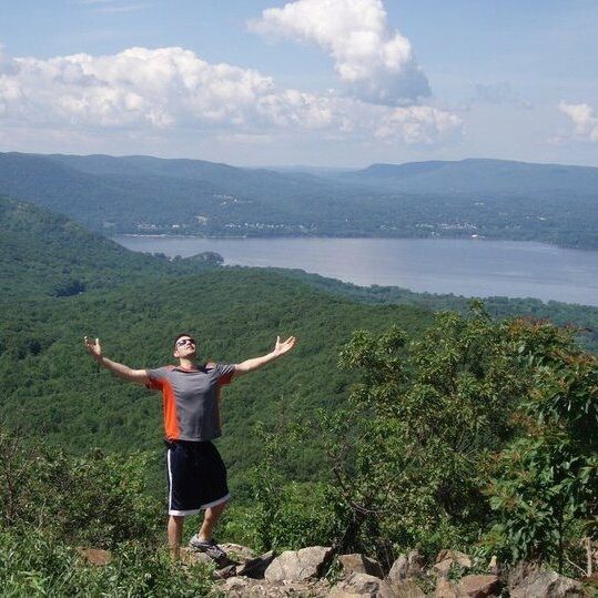 A man standing on top of a mountain with his arms in the air.